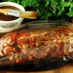 Mięso w torbie z marynatą, gotowe do przygotowania pysznego beef jerky. Obok miseczka z marynatą i pędzelek.