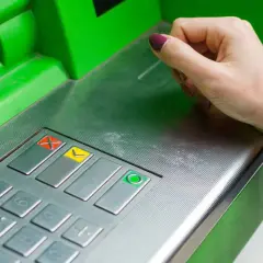 Eine Hand bedient ein grünes Geldautomaten-Bedienfeld. So funktioniert ein Bankwechsel: Geld abheben oder einzahlen.