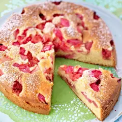 Ein saftiger Erdbeer Rhabarber Kuchen, bestäubt mit Puderzucker, wartet auf seinen Genuss. Ein Stück ist bereits herausgeschnitten.