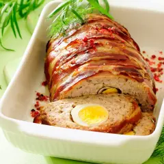 Najlepsza pieczeń rzymska, zawinięta w boczek, z jajkiem w środku, podana w białej brytfannie, ozdobiona ziołami i pieprzem.