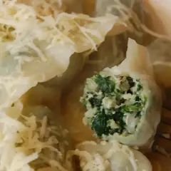Pyszne pierogi ze szpinakiem, polane sosem i posypane startym serem. Jeden pieróg jest przekrojony, ukazując soczyste nadzienie.