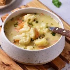 Kremowa zupa z kalafiora z marchewką i natką pietruszki, podana w misce na drewnianych deskach. Pyszne dania z kalafiora na chłodne dni.