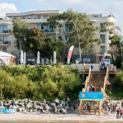 Hotel Lambert z tarasem i schodami prowadzącymi na plażę. Na schodach widać ludzi.