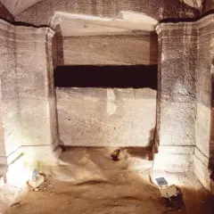 Wnętrze kamiennych katakumb, co to jest? Grobowce wykute w skale, z kamiennymi ławami i ciemnymi niszami.