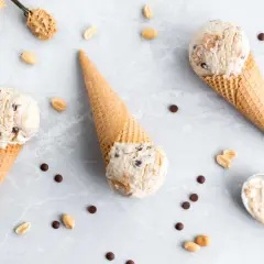 Drei Eiswaffeln mit cremigem Peanut Butter Cup Eis, umgeben von Erdnüssen und Schokostückchen.
