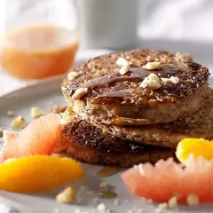 Pile de pancakes muesli, nappés de sirop et garnis de noix, accompagnés de quartiers d'agrumes.