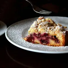 Ein Stück von Omas Kirschkuchen mit Streuseln, bestäubt mit Puderzucker, wartet auf seine Gabel.