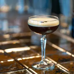 Elegancki drink z espresso, z gęstą pianką na wierzchu, stoi na błyszczącym blacie.