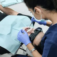 Dentystka w rękawiczkach zakłada pacjentowi na zęby materiał, być może formokrezol, do leczenia kanałowego.