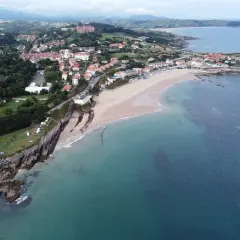 Vista aérea de la **playa de Comillas**, con sus casas, acantilados y el mar Cantábrico.