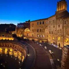 Il mercato di Traiano illuminato di notte, con le sue antiche mura di mattoni e l'arco semicircolare, evoca un'atmosfera magica.
