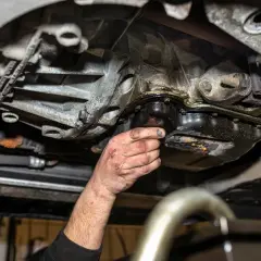 Ręka mechanika sprawdza szczelność miski olejowej. Widać wycieki oleju i zabrudzenia.