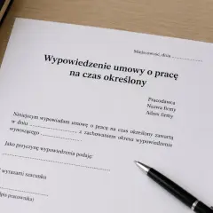 Dokument "Wypowiedzenie umowy o pracę na czas określony" leży na biurku obok długopisu.