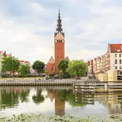 Elbląg i okolice co zobaczyć: malowniczy widok na rzekę z odbijającymi się kamienicami i wieżą kościoła. Idealne miejsce na spacer.