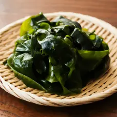 Wakame que es: algas marinas verdes y frescas en una cesta de bambú sobre una mesa de madera.