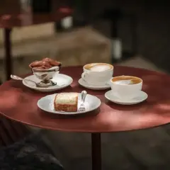 Två kaffekoppar med latte macchiato och en latte står på ett rött bord. Bredvid finns en bit kaka och en skål med chokladmousse.