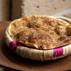 Manouche au zaatar, un délice croustillant aux épices, servi dans un panier tressé aux accents fuchsia.