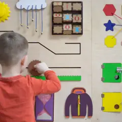 Chłopiec bawi się na tablicy sensorycznej, odkrywając świat przez doświadczenie. Widoczne są tam koła zębate, liczby i kształty.