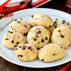Biscotti con gocce di cioccolato spolverati di zucchero a velo su un piatto bianco, pronti per essere gustati.