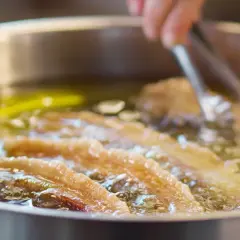 Almitas de Soria dorándose en aceite caliente. Unas pinzas metálicas manipulan la fritura.