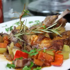 Zart gebratener kaninchen braten in der pfanne, serviert mit Kartoffeln, Karotten, Sellerie und Paprika, garniert mit Rosmarin.