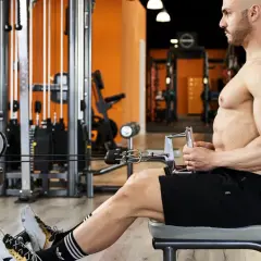 Uomo in palestra esegue un esercizio ai cavi, con le mani che afferrano la barra per le spinte in basso triangolo.