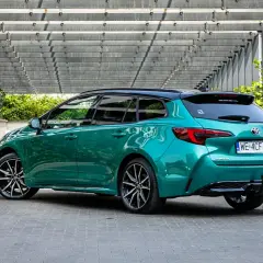 Zielona Toyota Corolla 2.0 Hybrid, kombi, z czarnym dachem, zaparkowana pod nowoczesną pergolą. Dane techniczne tego modelu są imponujące.