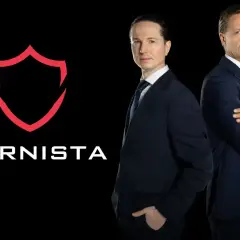 Dwóch mężczyzn w garniturach obok logo "KARNISTA" na czarnym tle.