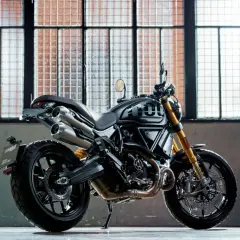 Czarny motocykl Ducati Scrambler 1100 Sport Pro, jeden z najlepszych motocykli, stoi przed industrialnymi oknami.