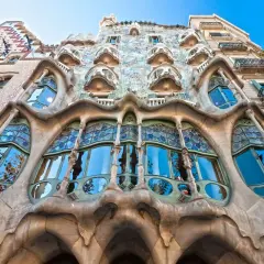 Façade d'un bâtiment à l'architecture organique, avec un **art nouveau motif végétal** sculpté dans la pierre et des vitraux bleus.