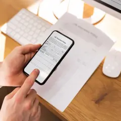 Dłoń trzyma smartfon, który działa jak darmowy skaner dokumentów, skanując polisę ubezpieczeniową.