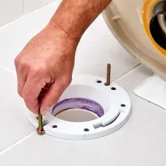 A hand tightens a bolt on a toilet flange installed on a tiled floor, preparing for a new toilet.