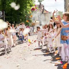 15 czerwca. Dzieci w białych strojach sypią kwiaty podczas procesji. W tle widać duchownych i wiernych.