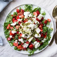 En fräsch sallad med jordgubbar, fetaost och pumpafrön på en vit tallrik.