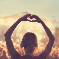 Ragazza fa un cuore con le mani a un concerto, immersa nell'atmosfera delle canzoni romantiche inglesi.