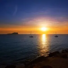 Un atardecer mágico en Ibiza, con veleros navegando y el sol tiñendo el mar de oro. Un lugar perfecto donde ver el atardecer en Ibiza.