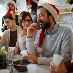 Fröhliche Menschen feiern Weihnachten. Sie tragen Weihnachtsmützen und trinken. Ist Heiligabend ein Feiertag? Ja, und sie genießen ihn!
