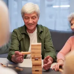 Un homme âgé sourit en retirant un bloc d'une tour Jenga. Un jeu stimulant pour la mémoire, utile dans le cadre d'un jeu Alzheimer.