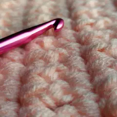 Uncinetto rosa su tessuto lavorato a maglia color pesca, mostrando la differenza tra uncinetto e ferri.