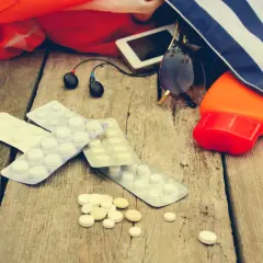 Medikamente gegen Kreislaufprobleme bei Hitze liegen neben Sonnencreme, Sonnenbrille und Kopfhörern auf Holz.