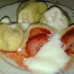 Pyszne pierogi z truskawkami, polane śmietaną i posypane cukrem, kuszą swoim wyglądem i zapachem.