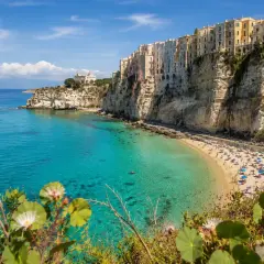A vibrant beach scene on the Calabria coast, with colorful buildings perched on dramatic cliffs overlooking turquoise waters.