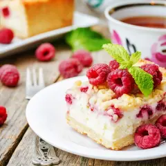 Malinowa chmurka z serem i malinami, udekorowana listkiem mięty, na talerzyku obok filiżanki herbaty.