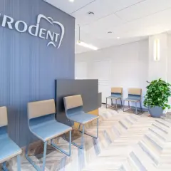 Nowoczesna poczekalnia gabinetu stomatologicznego z logo "Eurodent", krzesłami i rośliną.