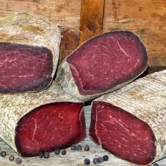 Quatre morceaux de viande des Grisons, d'origine suisse, sont présentés sur un fond de bois. La viande est rouge foncé, avec une texture fibreuse.