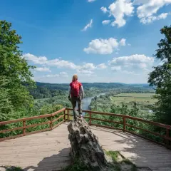 Kobieta z plecakiem podziwia widok na dolinę rzeki. Idealne miejsce, by zastanowić się, gdzie w Bieszczady wybrać się na wędrówkę.