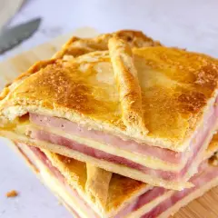 Dos porciones de empanada de jamón y queso apiladas, con masa dorada y relleno visible.