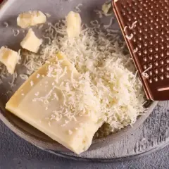 Kawałek sera Padano i świeżo starty ser na talerzu, obok miedziana tarka.