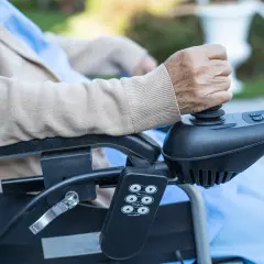 Dzieci na wózku inwalidzkim, starsza osoba trzyma joystick elektrycznego wózka, kontrolując ruch.