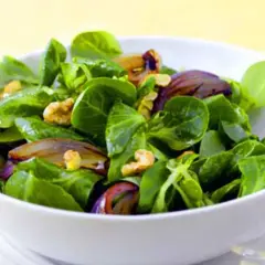 Ein frischer Feldsalat mit knackigen Zwiebeln und Walnüssen in einer weißen Schüssel.